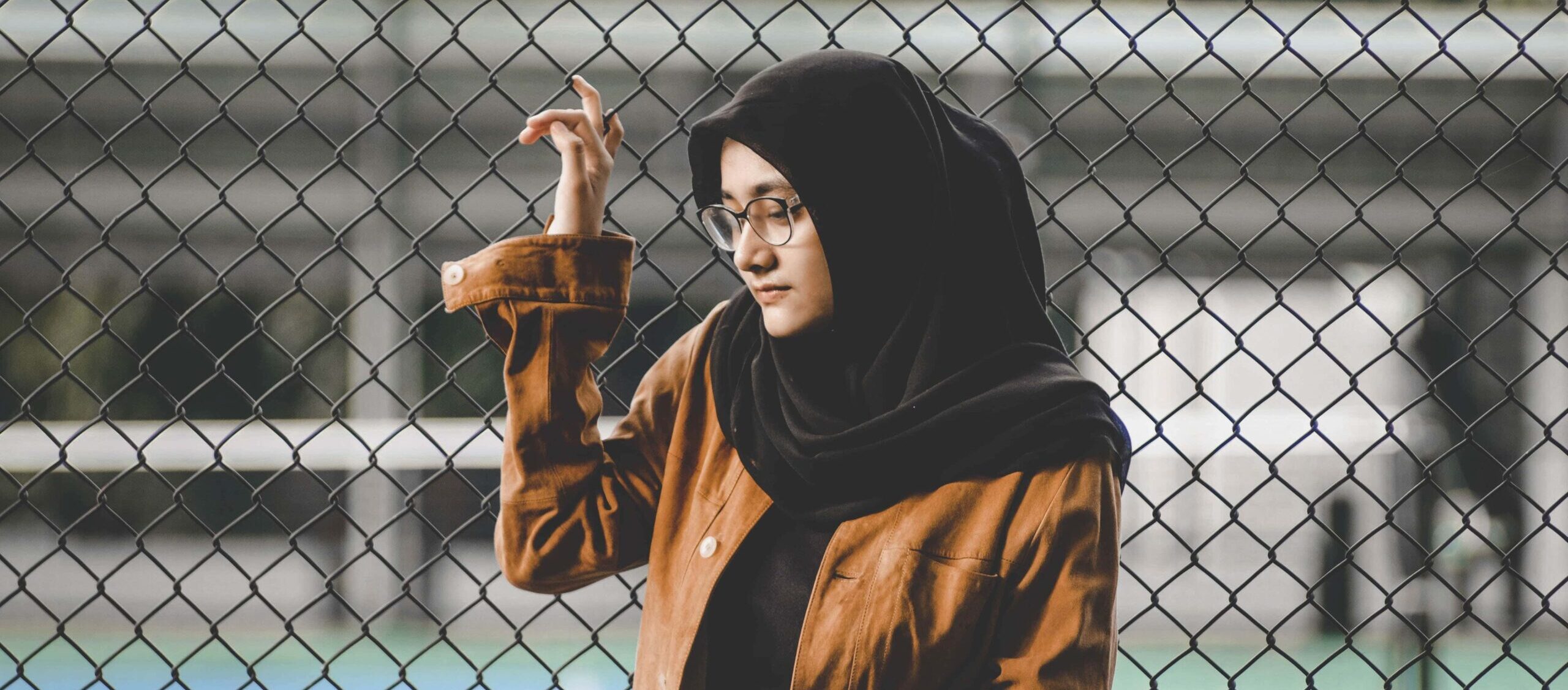 hijabi woman holding onto wire fence