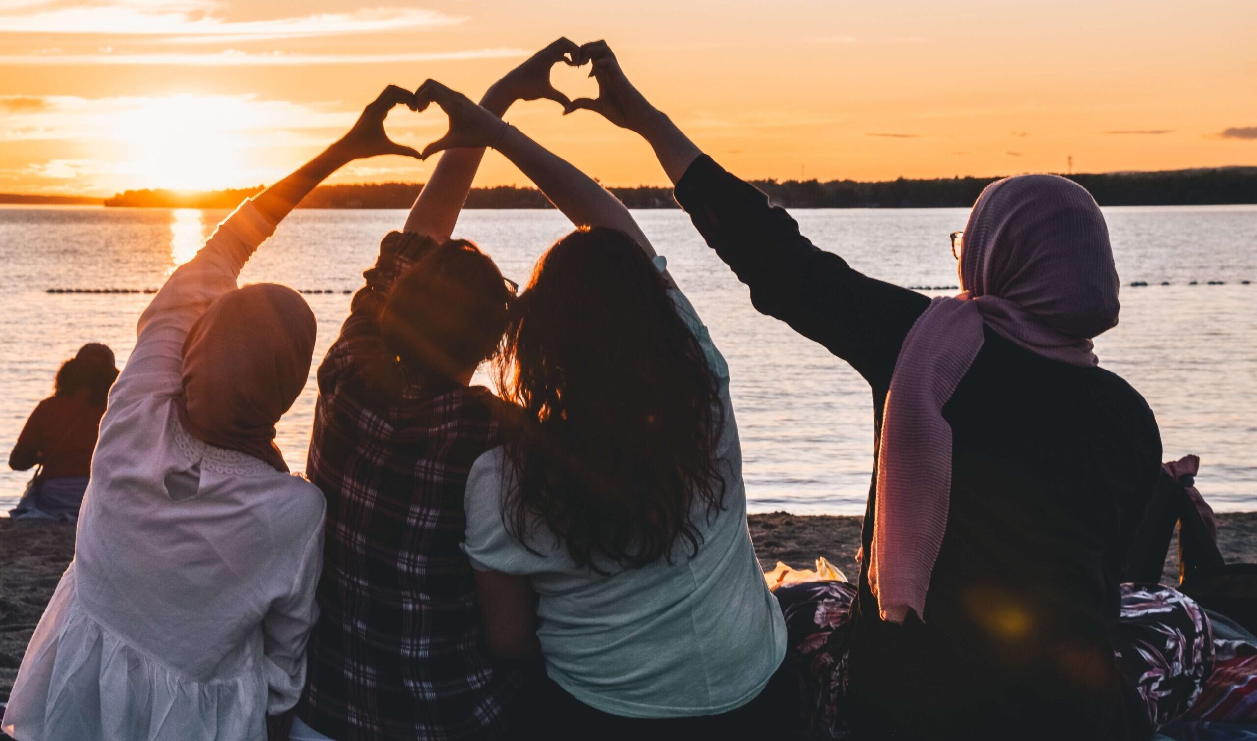 people looking at sunset making heart shapes with their hands in the air