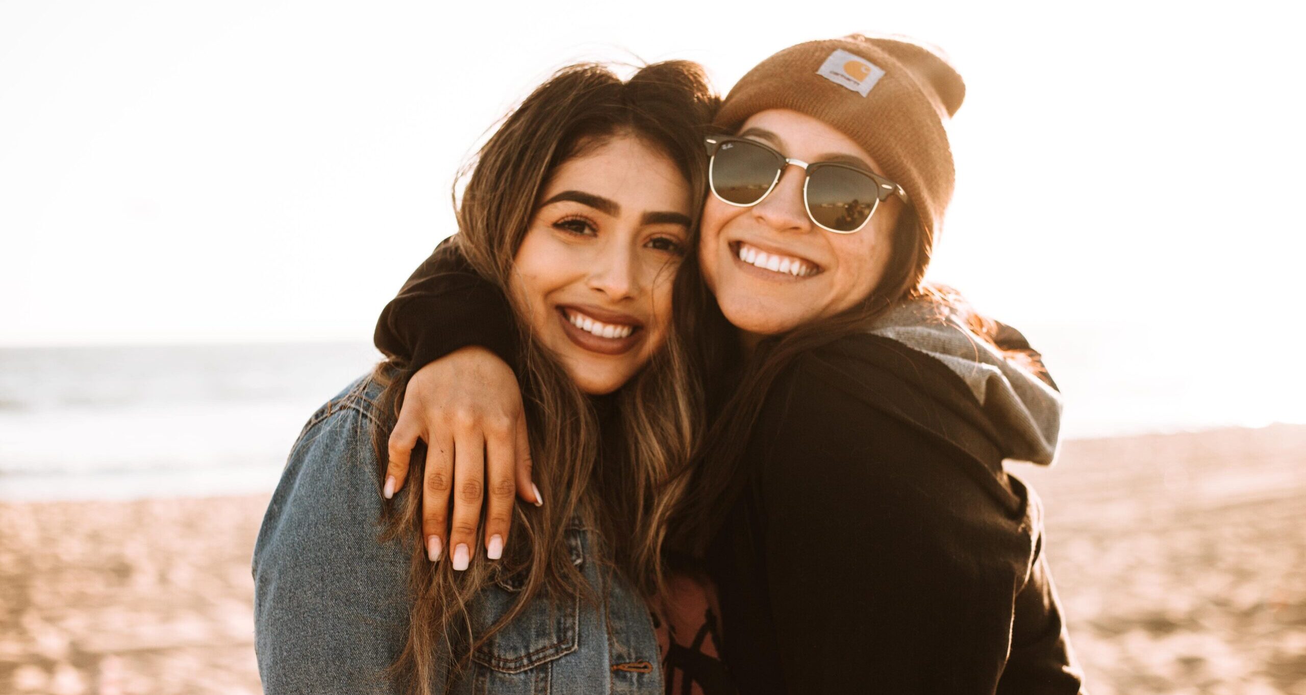 two girls hugging on beach, smiling